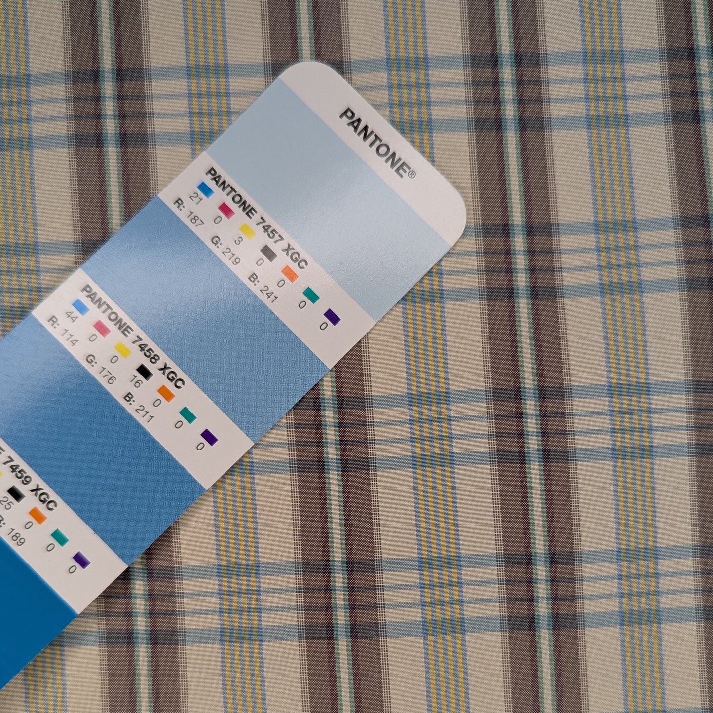 Off-white background with multicolored plaid pattern woven into fabric. Yarn dyed silk. Photographed with a blue pantone chip for reference and color matching.