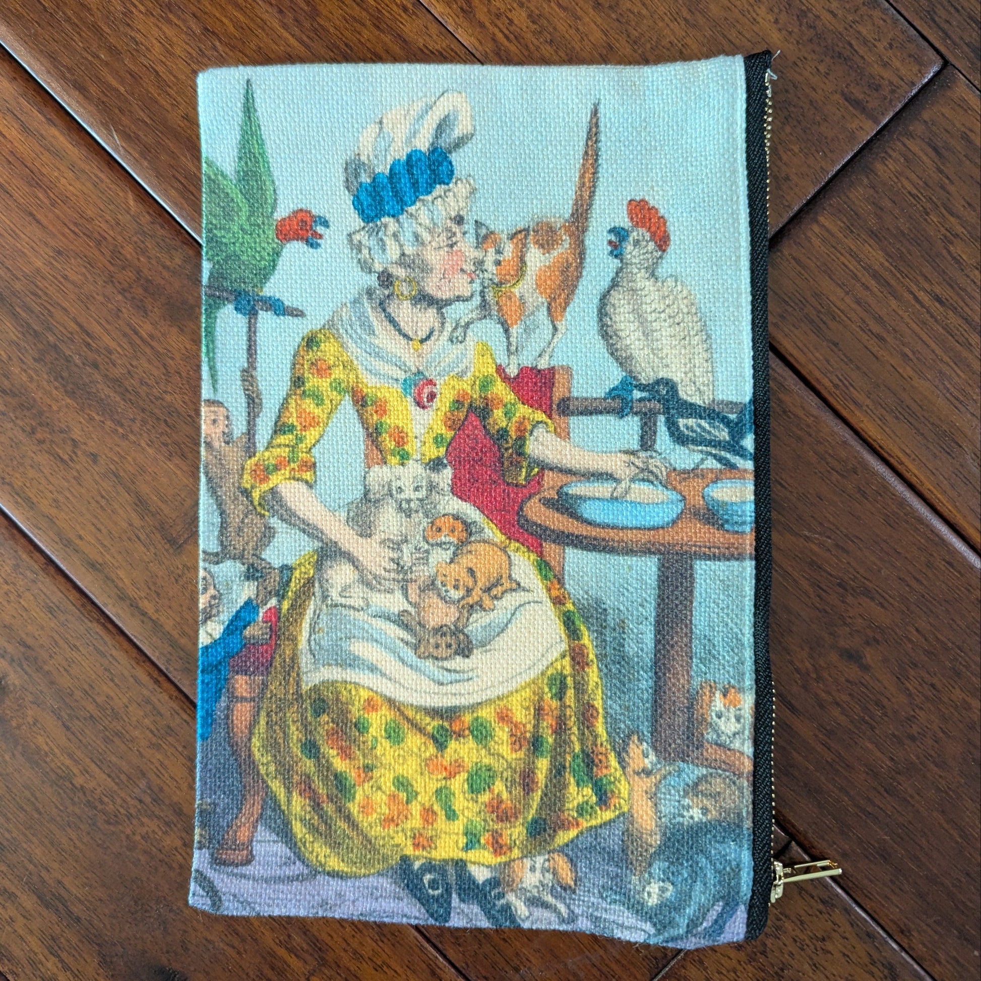 Large zipper pouch printed a woman surrounded by birds, cats, dogs, puppies and kittens while wearing a brightly colored yellow orange and green spotted dress and tall white cap with blue ribbon. From the 1790s. Virgil's Fine Goods