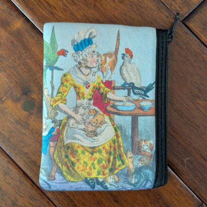 Small zipper pouch printed a woman surrounded by birds, cats, dogs, puppies and kittens while wearing a brightly colored yellow orange and green spotted dress and tall white cap with blue ribbon. From the 1790s. Virgil's Fine Goods