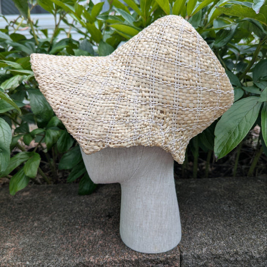 Side View Tan and white Straw bonnet with squared crown and open brim for regency era. Background of green peony leaves. VirgilsFineGoods.com
