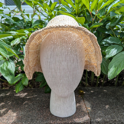 Side View Tan and white Straw bonnet with squared crown and open brim for regency era. Background of green peony leaves. VirgilsFineGoods.com