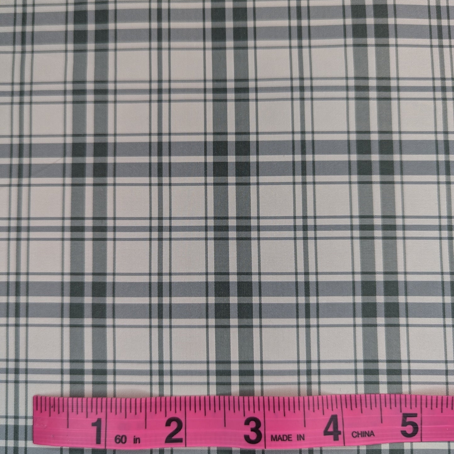 Off-white background with green plaid pattern woven into fabric. Yarn dyed silk. Photographed with a pink ruler to illustrate pattern scale.