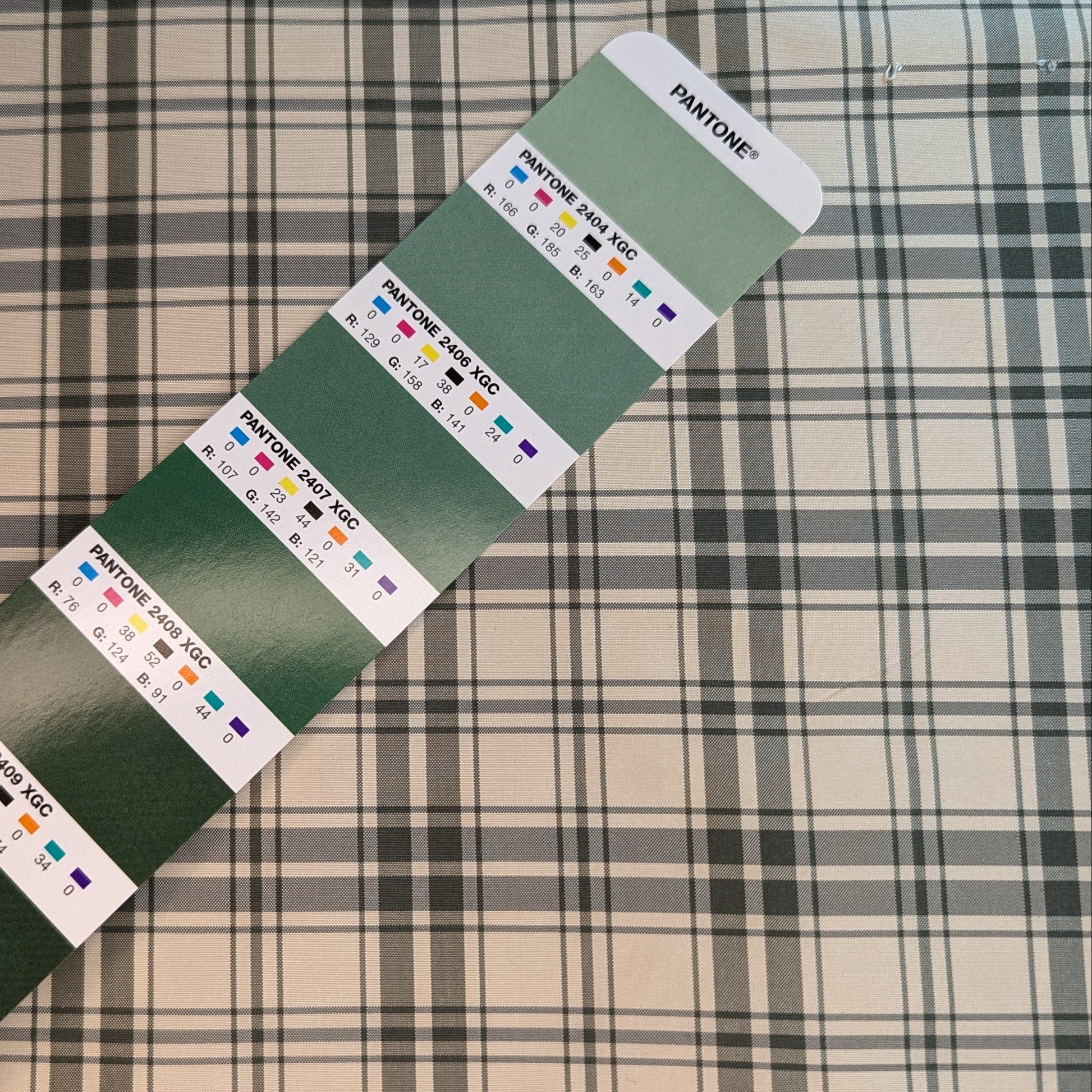 Off-white background with green plaid pattern woven into silk fabric. Yarn dyed silk. Photographed with a pantone chip for reference and color matching.
