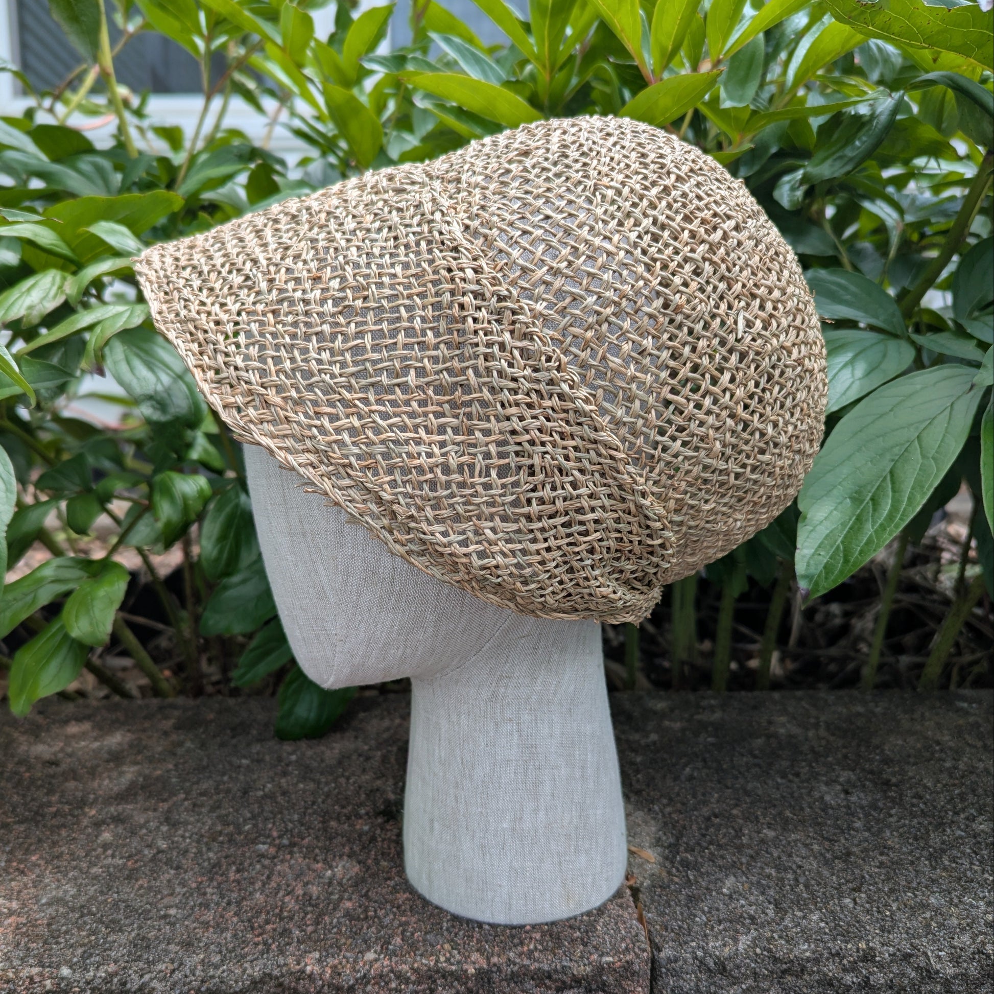 Tan Open-weave Straw bonnet with short brim rounded crown for early regency era. Background of green peony leaves. VirgilsFineGoods.com