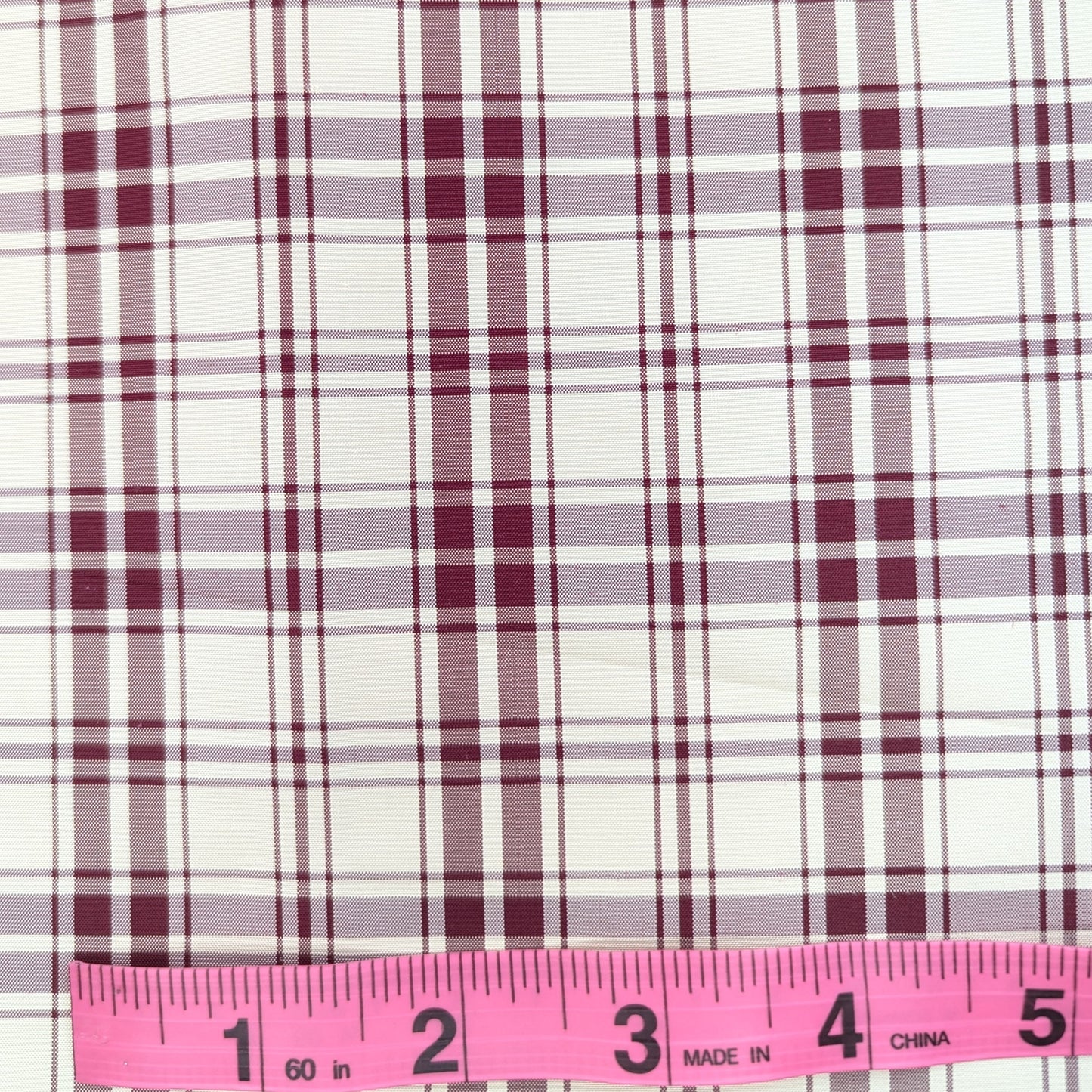 Off-white background with red plaid pattern woven into fabric. Yarn dyed silk. Photographed with a pink ruler to illustrate pattern scale.