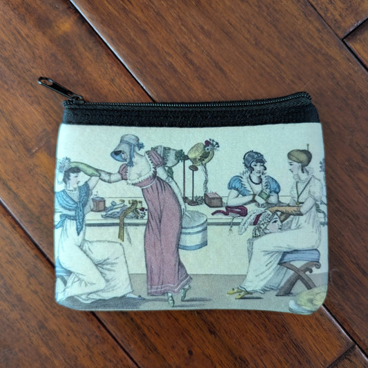 Small pouch printed with 3 women from the 19th century with several women trying on hats in a shop. Virgil's Fine Goods