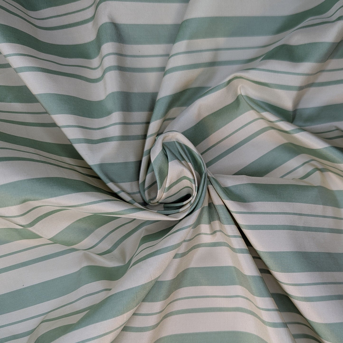 Off-white background with sage green stripe pattern woven into fabric. Yarn dyed silk. Photographed after being swirled to show weight and drape of fabric