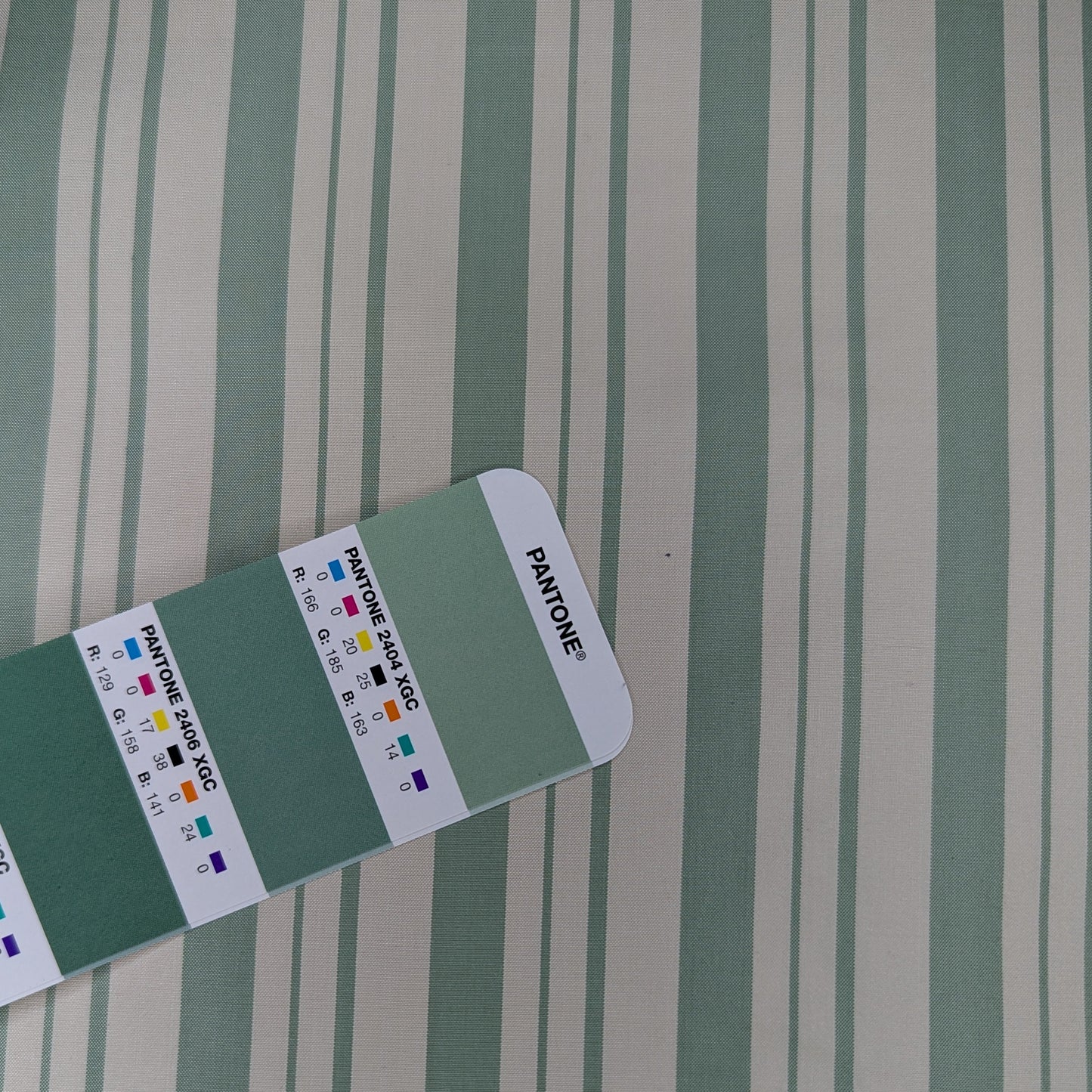 Off-white background with sage green stripe woven into fabric. Yarn dyed silk. Photographed with pantone chip for color reference and matching.