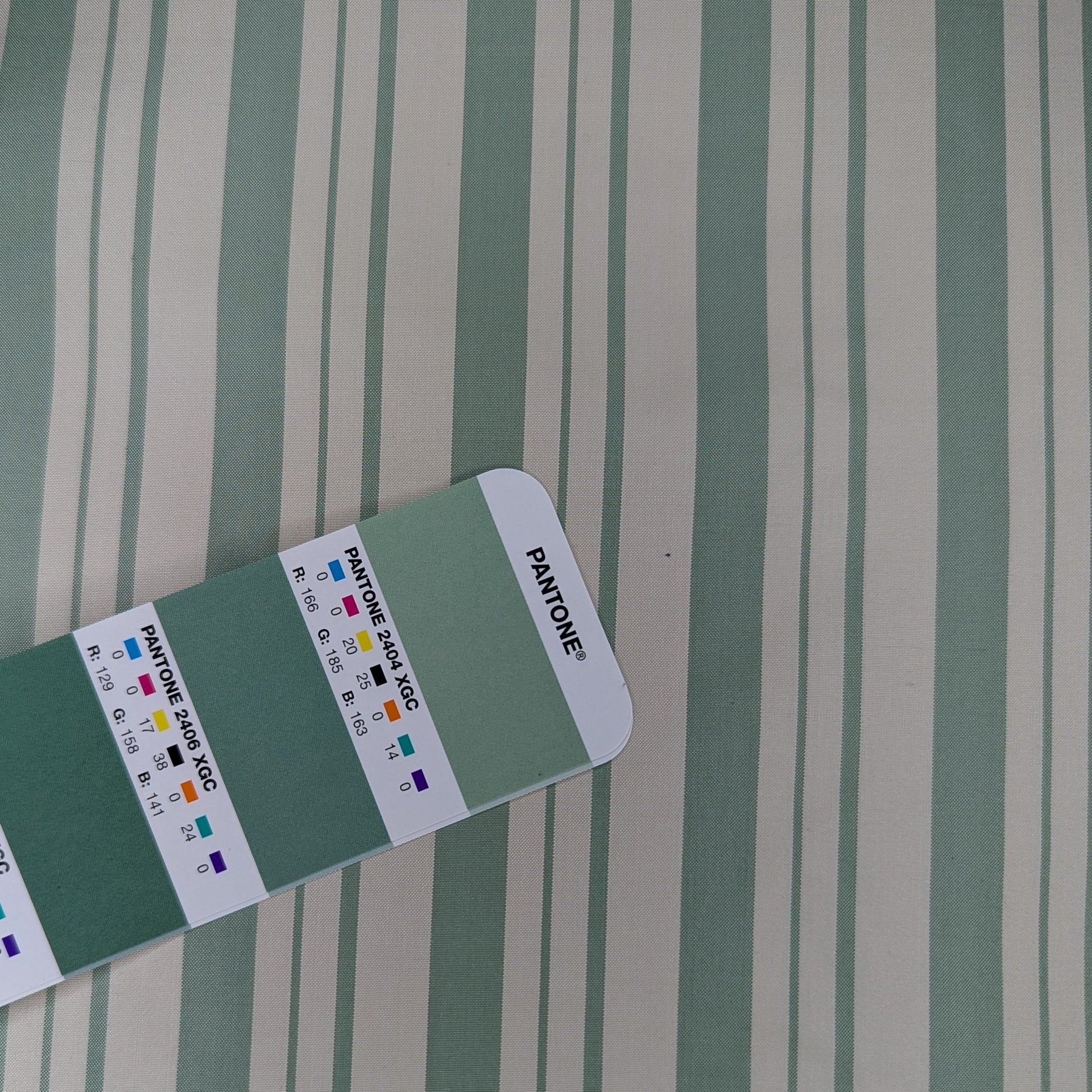 Off-white background with sage green stripe woven into fabric. Yarn dyed silk. Photographed with pantone chip for color reference and matching.