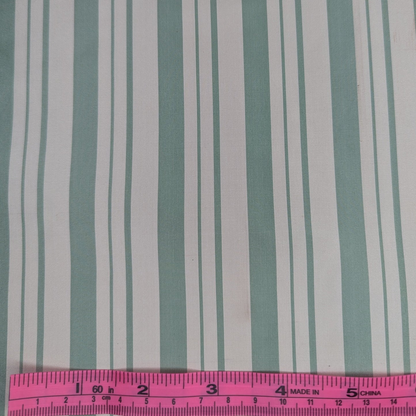 Off-white background with sage green stripes woven into fabric. Yarn dyed silk. Photographed with a pink ruler to illustrate pattern scale.