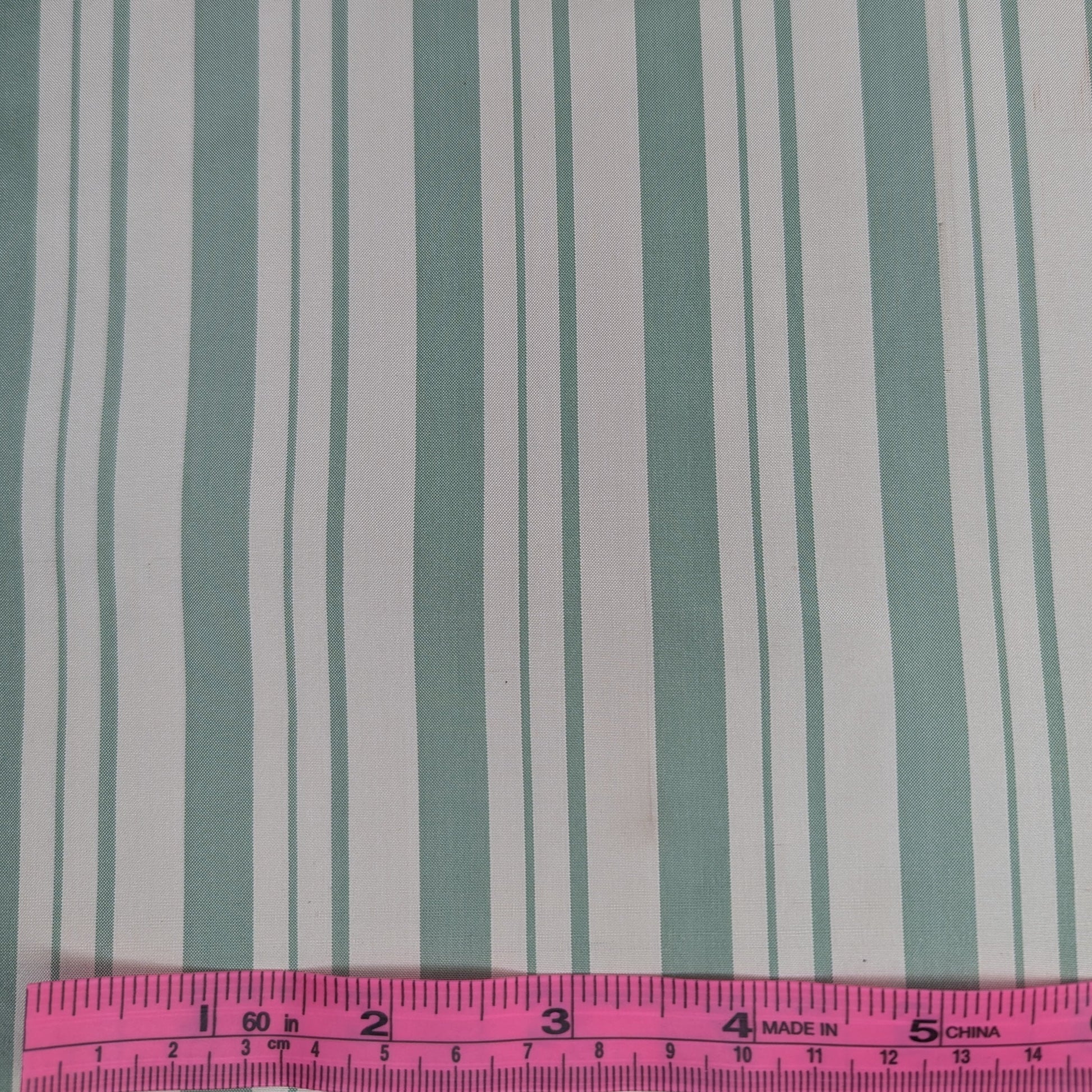 Off-white background with sage green stripes woven into fabric. Yarn dyed silk. Photographed with a pink ruler to illustrate pattern scale.