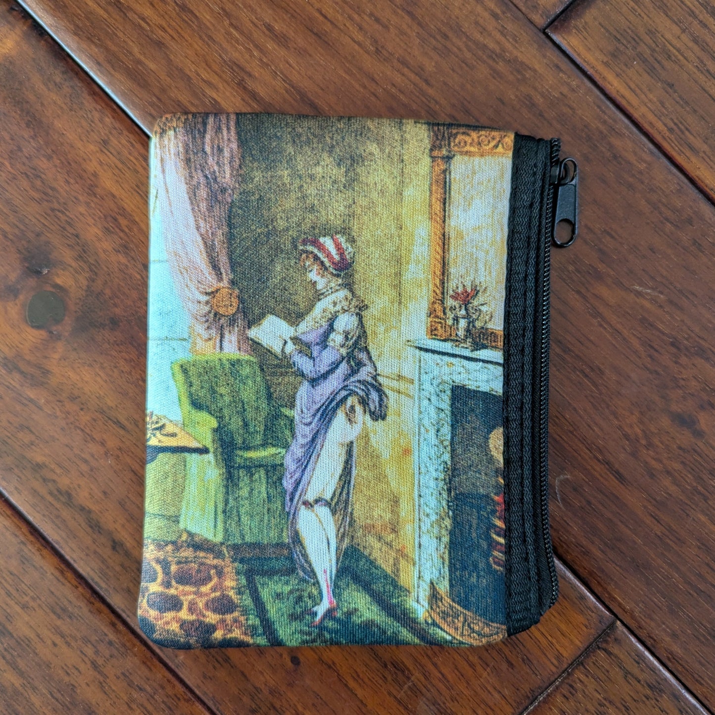 Small zipper pouch printed a woman reading and also lifting her skirt in the back, revealing her bare bum, to warm by the fire in a living room. From the 19th century with a purple dresses and brightly colored room. Virgil's Fine Goods
